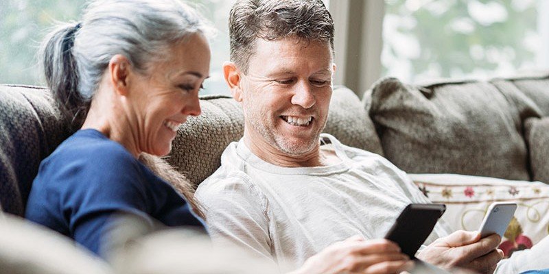 Older couple sat at home on a sofa smiling