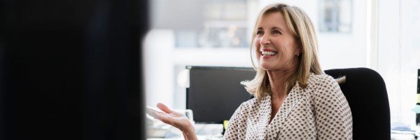 Smiling middle-aged woman enjoys a conversation with a colleague in her office.