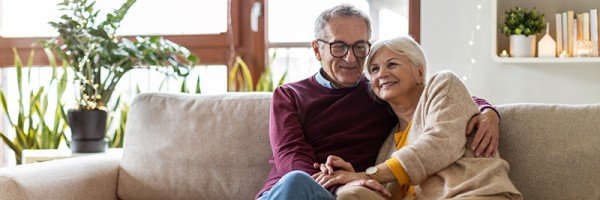 Retired couple sat at home on a sofa smiling