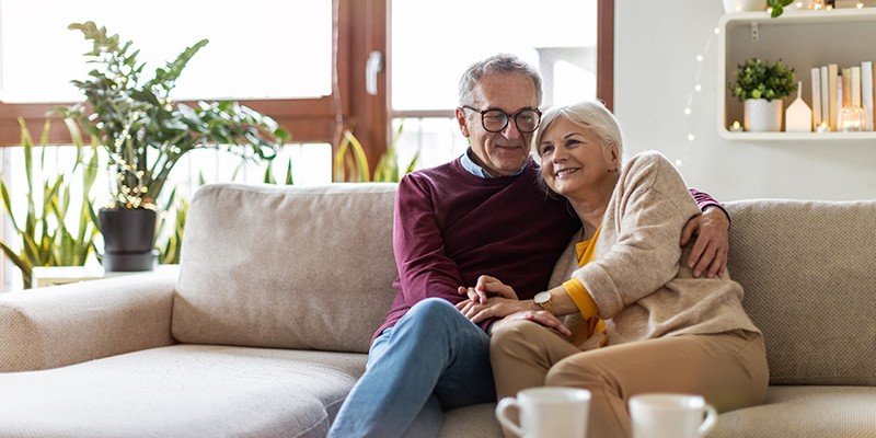 Retired couple sat at home on a sofa smiling